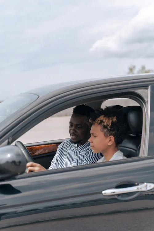 Driving instructor guiding a teen student through a behind-the-wheel lesson in a sedan.