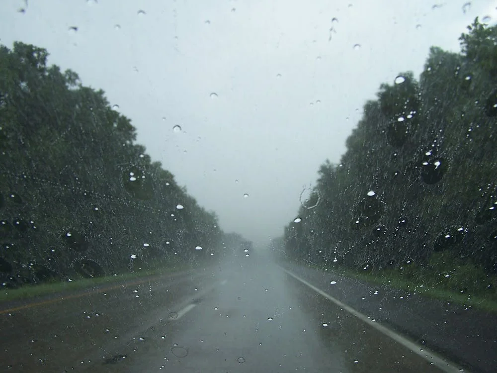 Rain streaking across a windshield while driving on a wet highway at dusk.