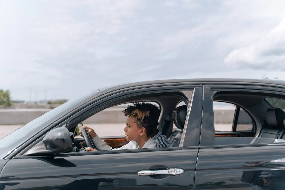Focused teen driver in a brown jacket watching the road, both hands on the steering wheel.